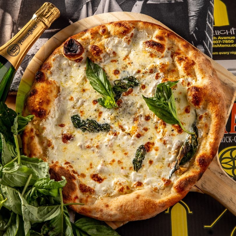 A white pizza with basil leaves and a bottle of Perrier-Jouët champagne on a wooden board.