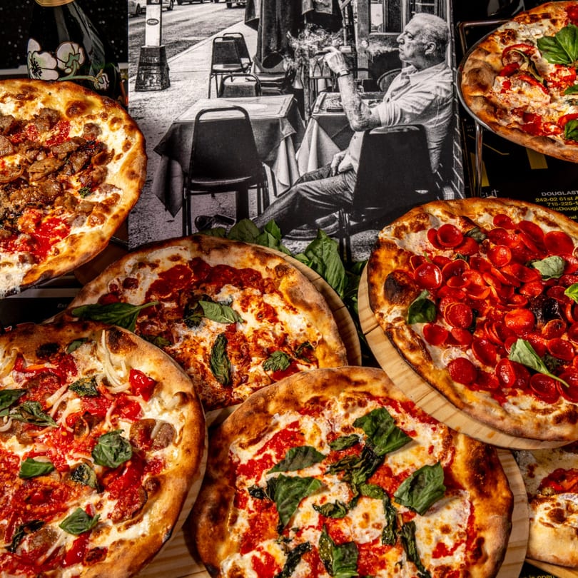 Assortment of Brooklyn Born pizzas, including pepperoni, sausage, and Margherita, on wooden boards.