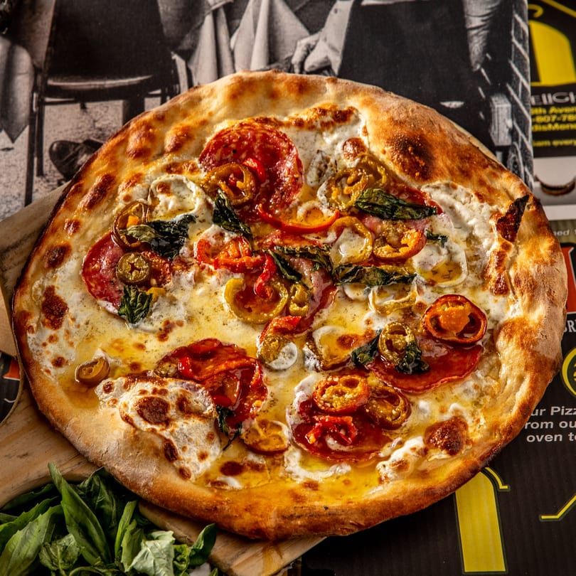 Brooklyn Born pizza with pepperoni, peppers, basil, and ricotta cheese on a wooden board.